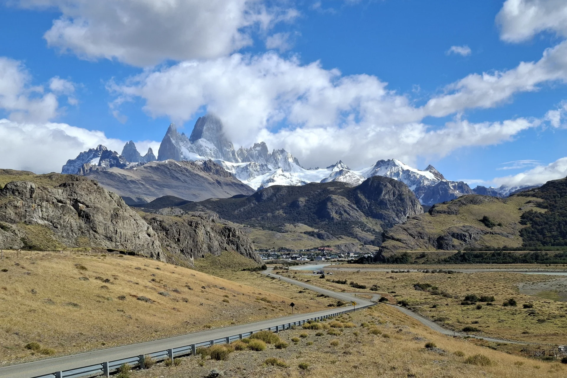 S'aprecia un paisatge de muntanya. El cel és clar, pel terreny una carretera serpenteja fins arribar al poble.