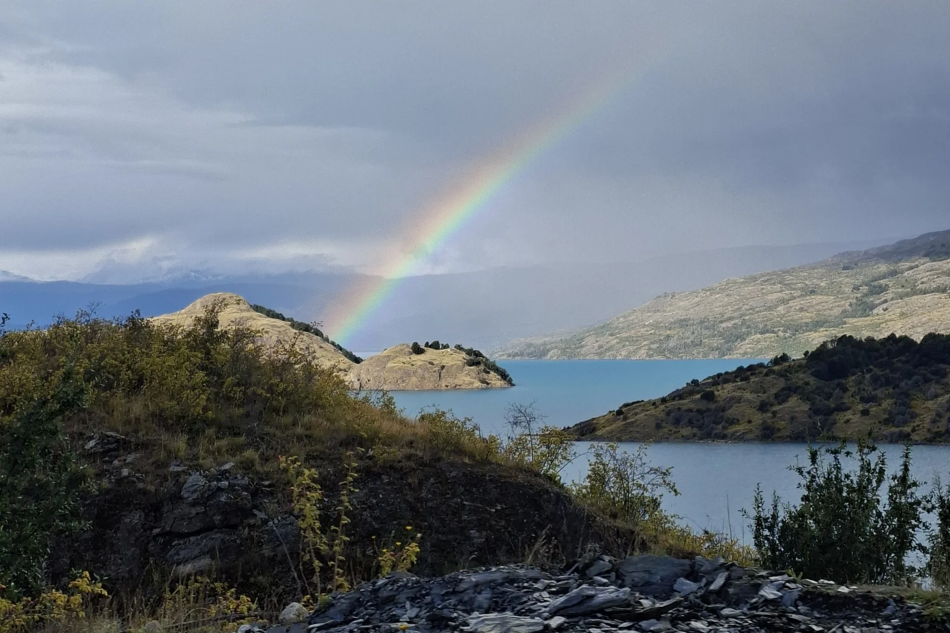 Un petit fragment de la carretera austral, amb molt de verd, muntanya, un llac i un arc de sant martí.