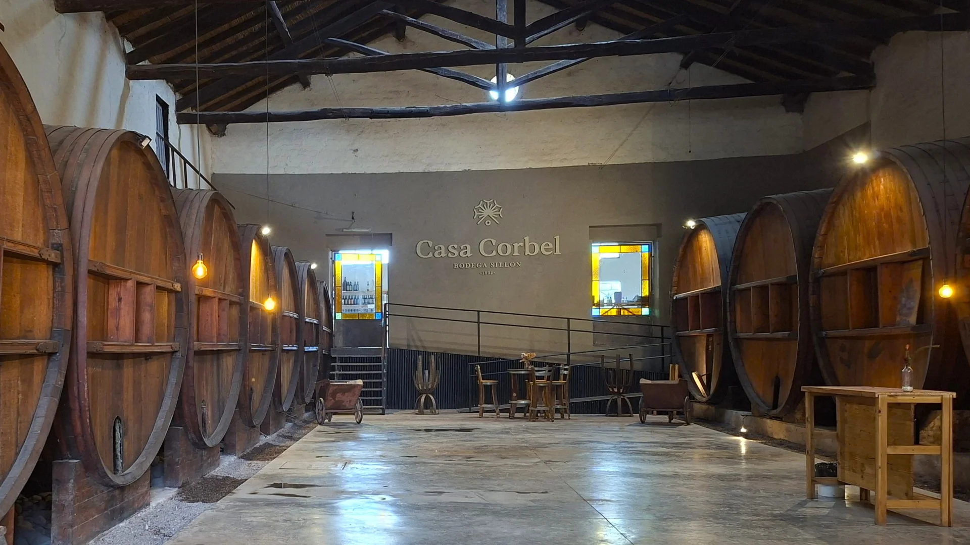 Vista interior de la Bodega Sillon (Casa Corbel), que mostra una gran sala amb terra polit i fileres de bótes de vi de fusta de grans dimensions a ambdós costats, sota un sostre de bigues de fusta.