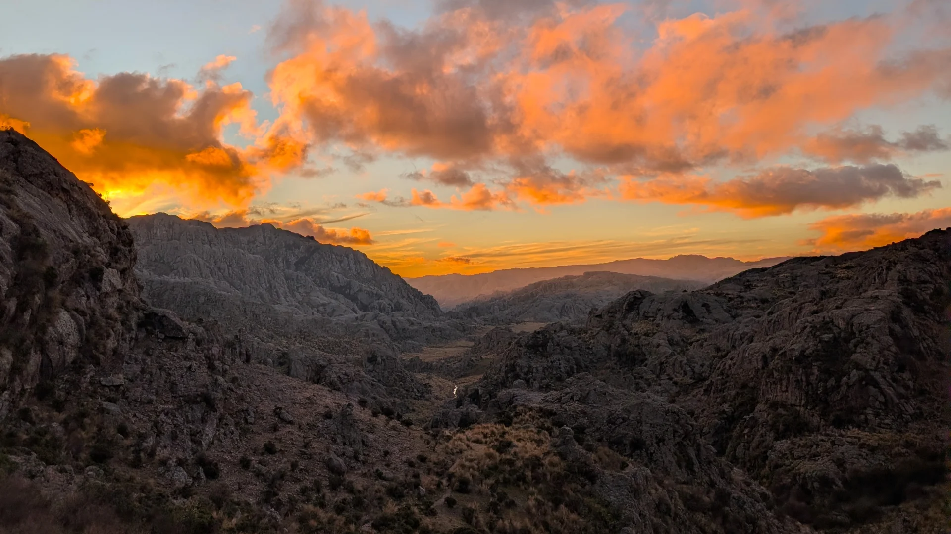 Vista panoràmica d'una posta de sol espectacular a Los Gigantes, amb els núvols il·luminats de colors taronja i daurat intensos sobre una vall profunda flanquejada per muntanyes rocoses en ombra.