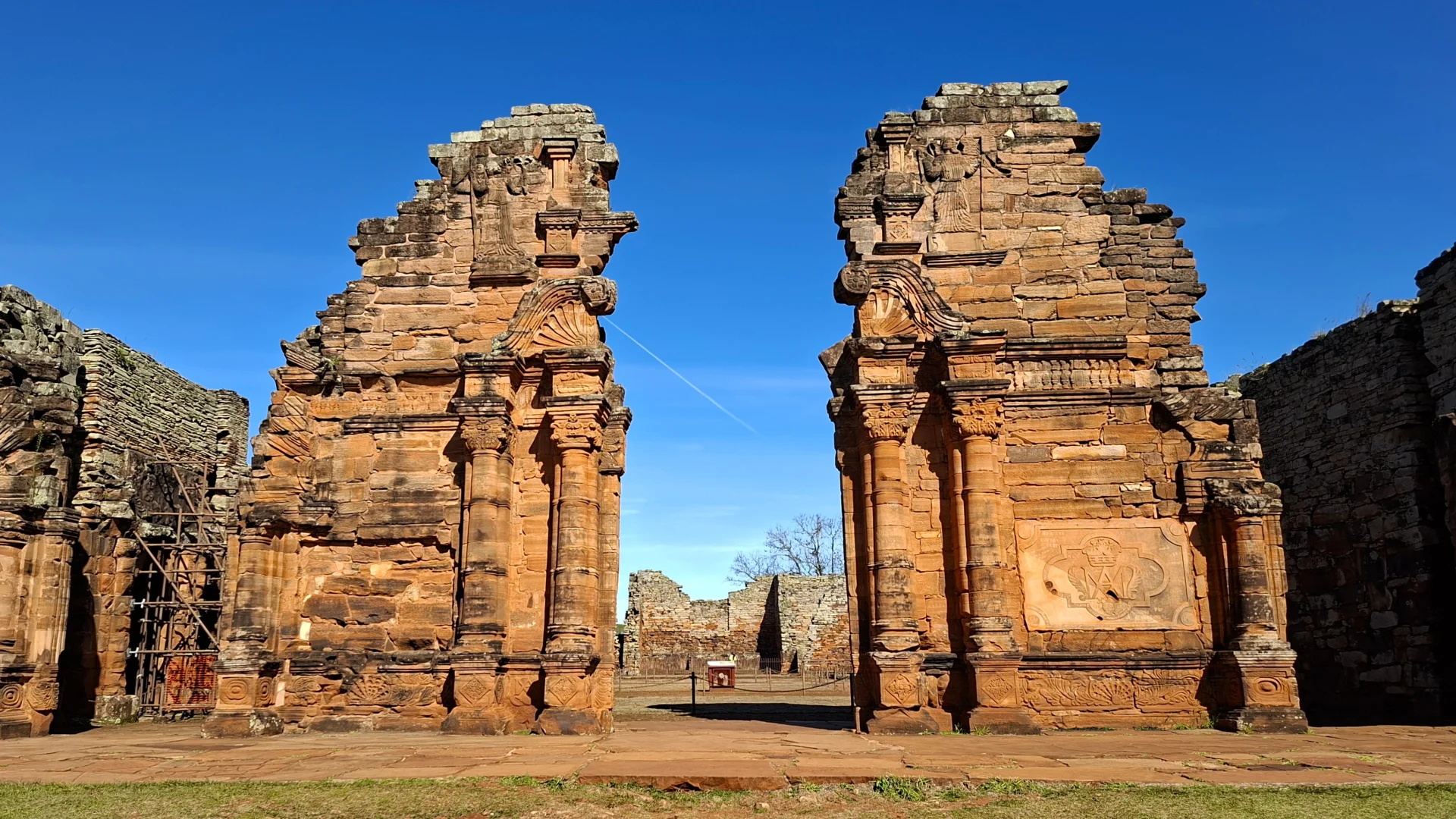 Les monumentals ruïnes de pedra vermellosa del portal d'entrada de l'església jesuítica de San Ignacio Miní, que destaquen per les seves columnes i motius esculpits sota un cel blau radiant.
