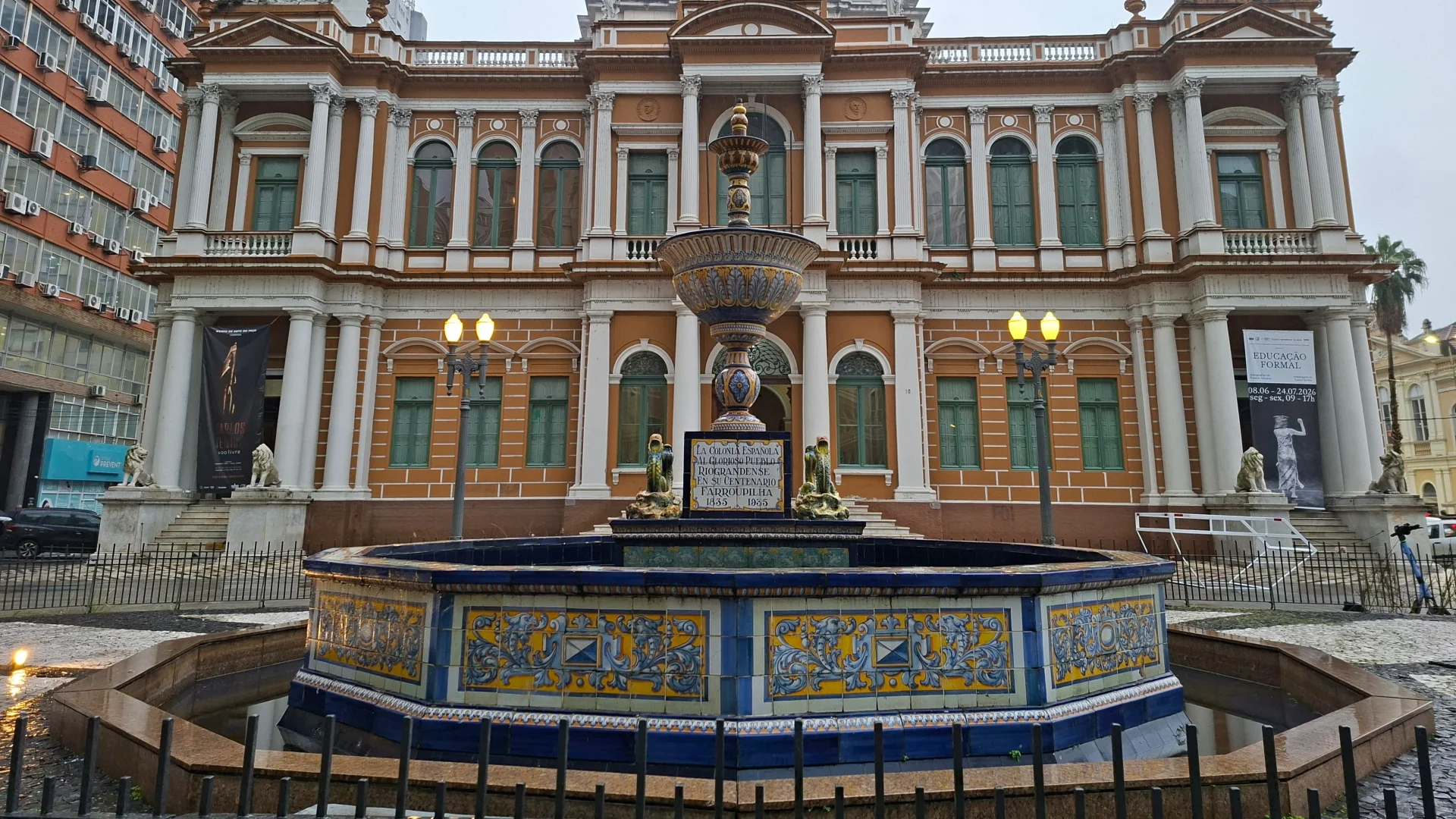 La font ornamental Talavera de la Reina, decorada amb rajoles de ceràmica blaves i grogues, situada a la plaça davant de la façana clàssica de l'edifici del Paço Municipal de Porto Alegre sota un cel ennuvolat.