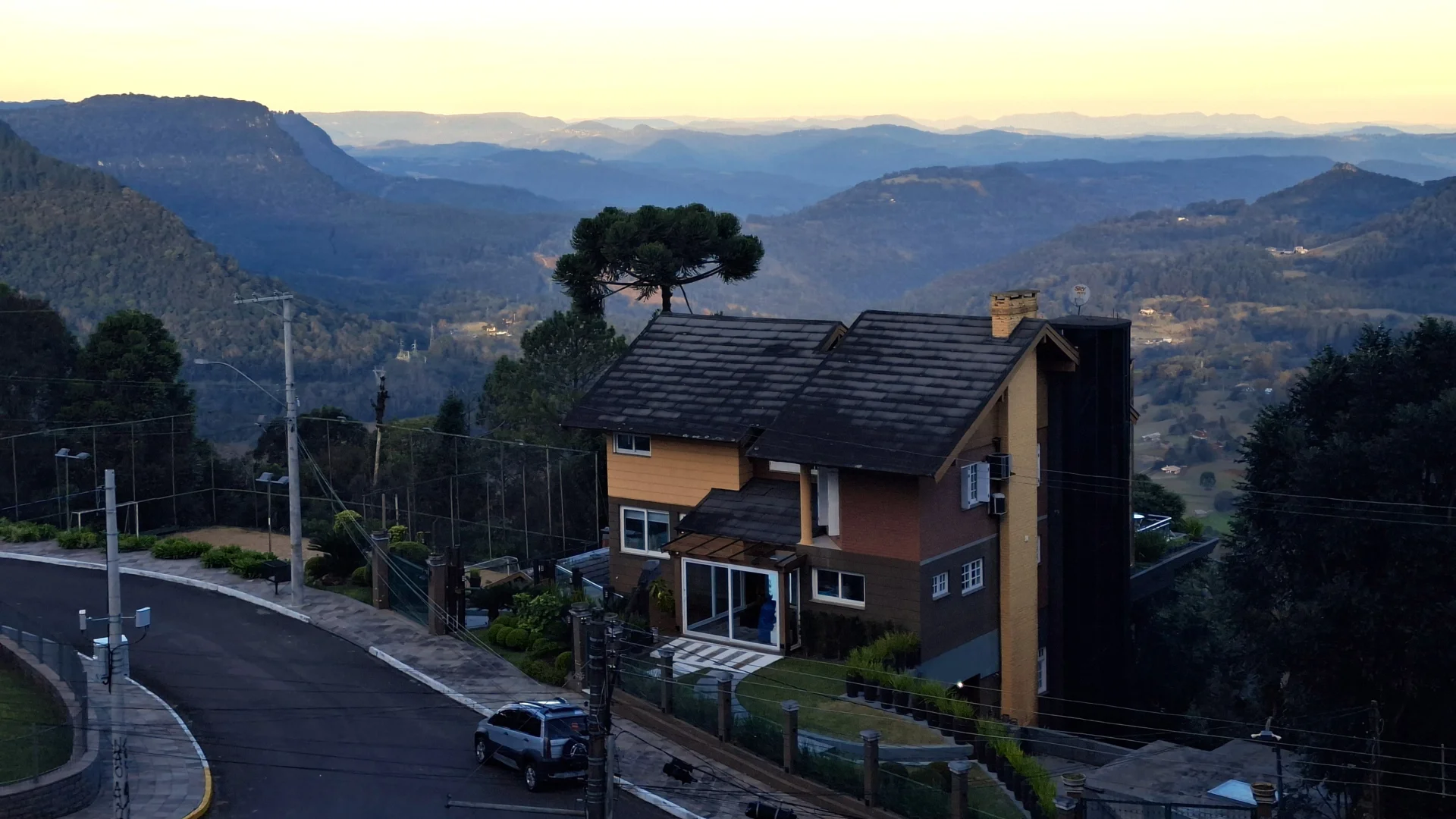 Vista panoràmica des d'un mirador a la serra, amb una casa de fusta d'estil alpí en primer pla i una extensa vall de turons verdosos que s'estén cap a les muntanyes a l'horitzó durant el capvespre.