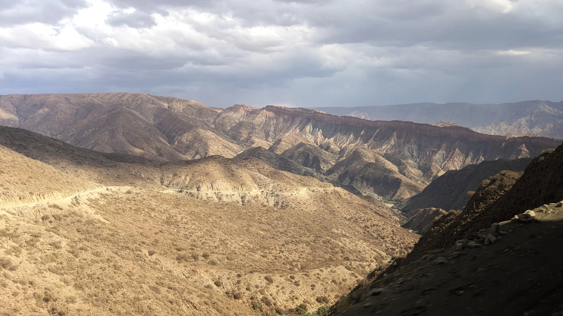 Vista panoràmica de la sinuosa carretera de muntanya entre Villazón i Tarija, mostrant una estreta pista que voreja el precipici a través de muntanyes àrides i escarpades que cauen cap a un profund barranc, sota un cel amb núvols i jocs d'ombres sobre el relleu.