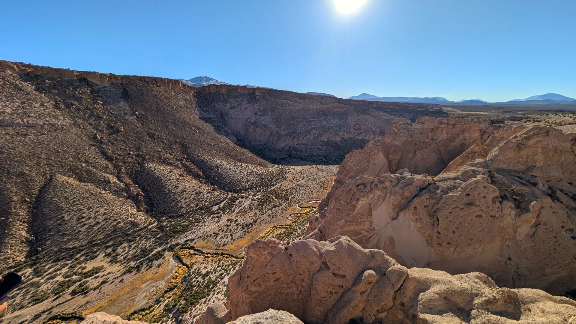 Vista aèria en perspectiva des del mirador del Cañón de la Anaconda, mostrant un profund congost de formacions rocoses escarpades per on serpenteja un estret rierol flanquejat per vegetació daurada, sota la intensa llum del sol en un cel net.